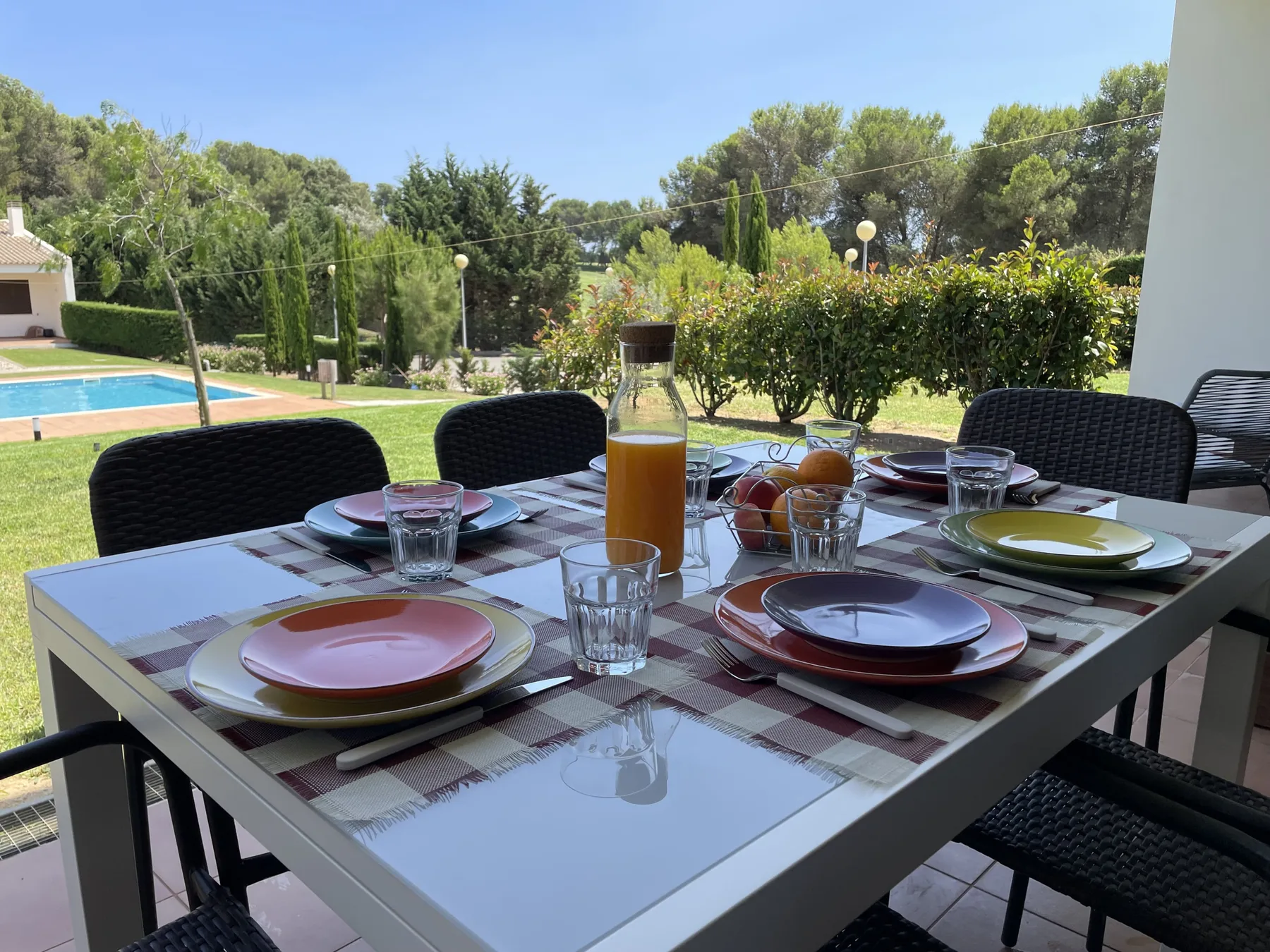 An outdoor dining table is set with plates and glasses beside a garden.