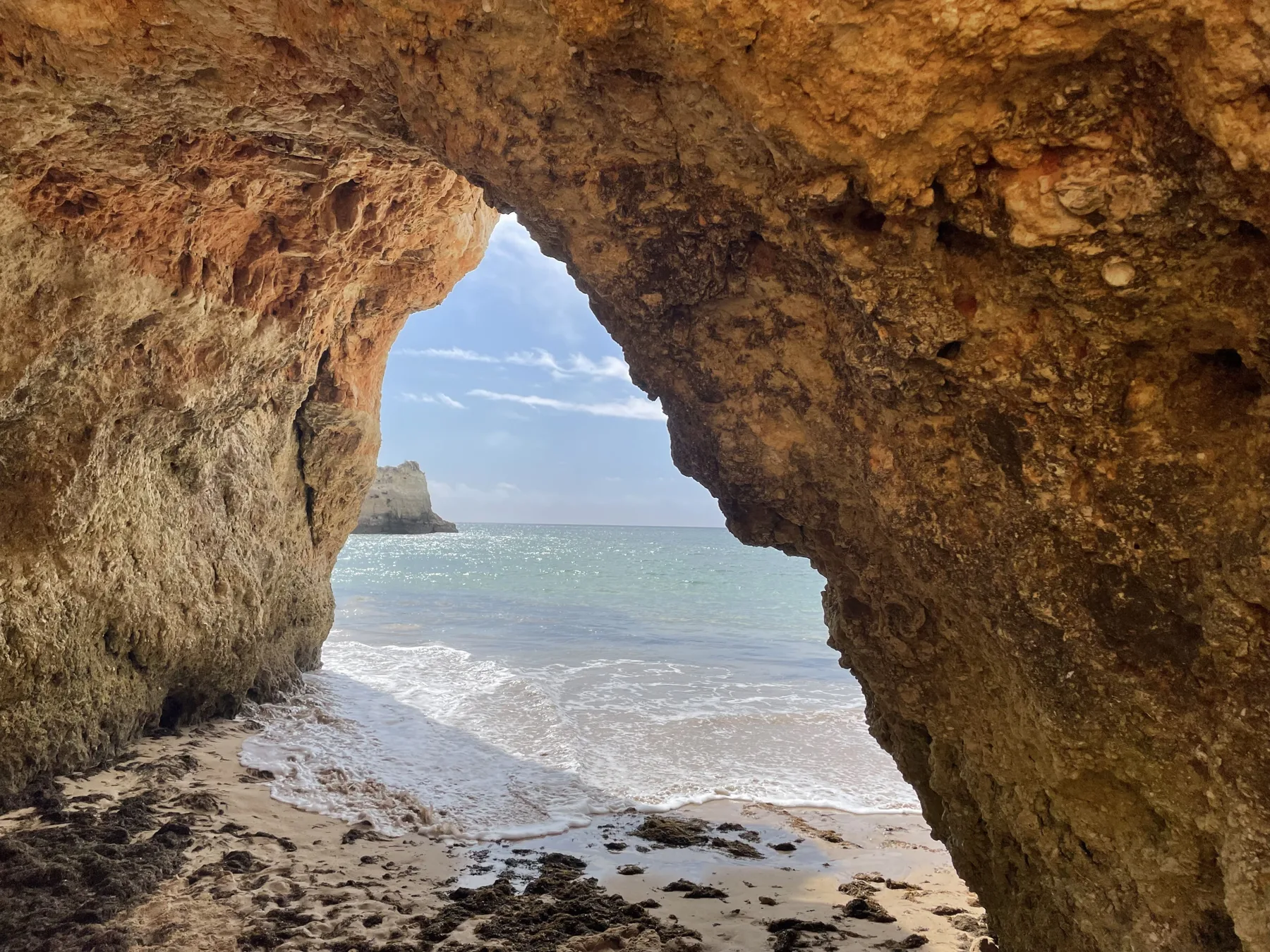 A rocky seaside cave opens onto a sandy beach and the ocean.