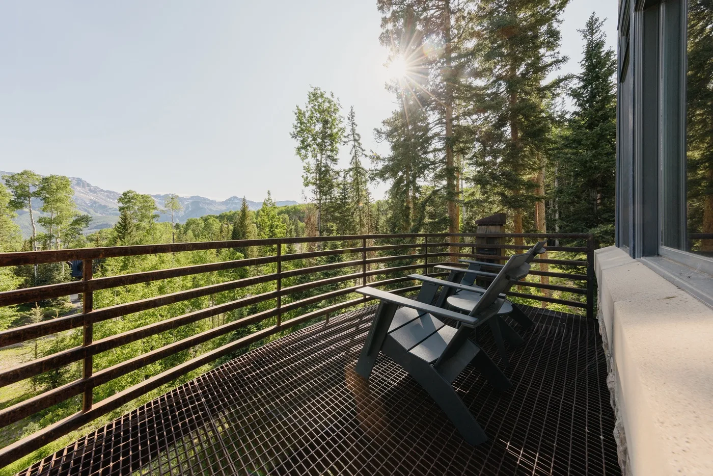 A deck with outdoor seating overlooks a forested mountain landscape.