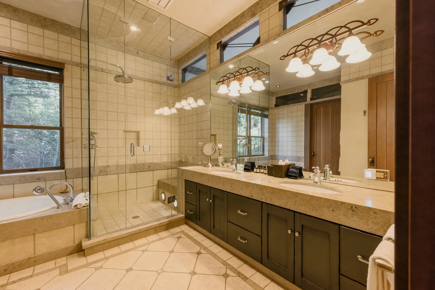 A spacious bathroom with a glass shower and a long vanity beneath illuminated mirrors.