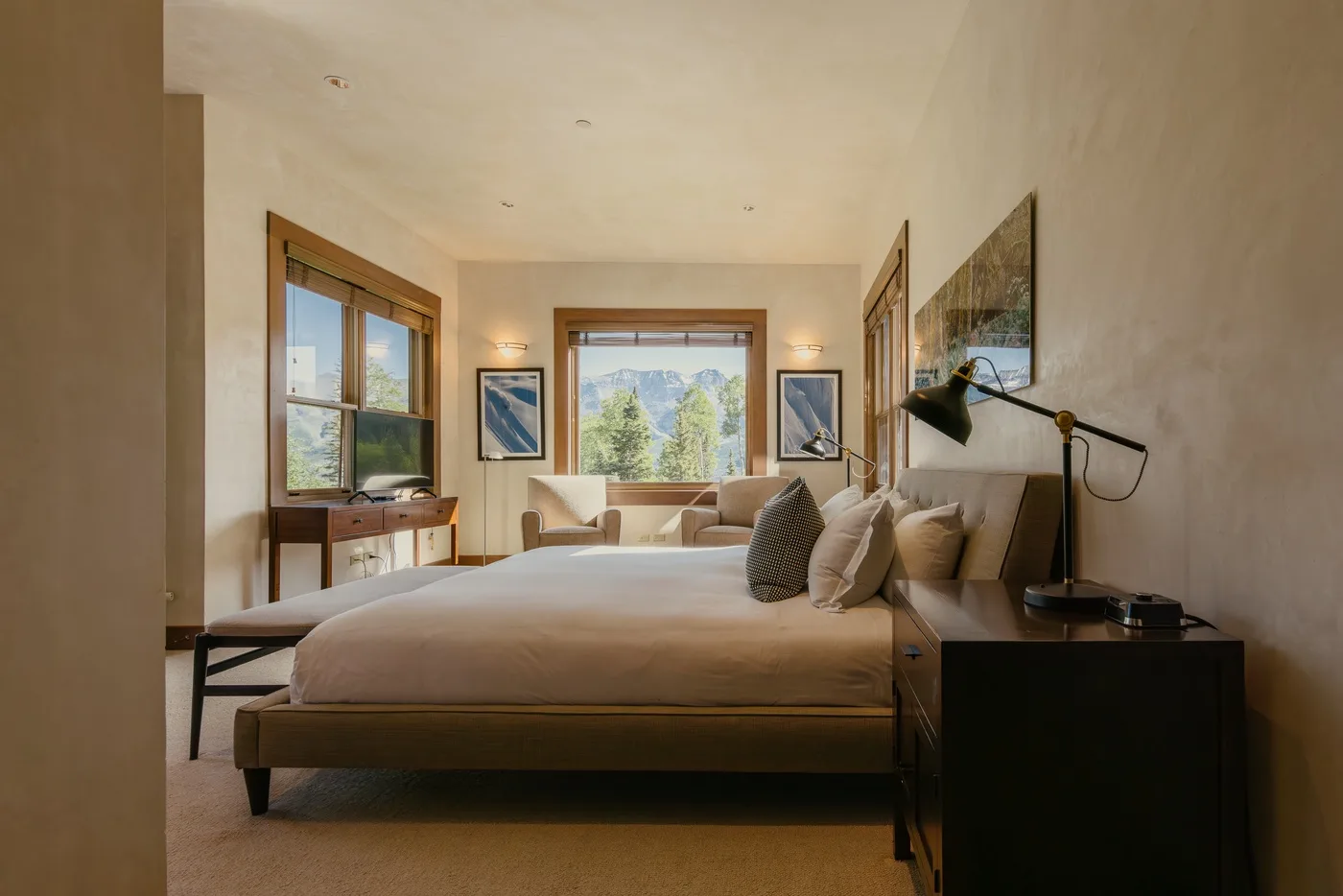 A bedroom with a large bed, bedside table, and windows overlooking greenery.