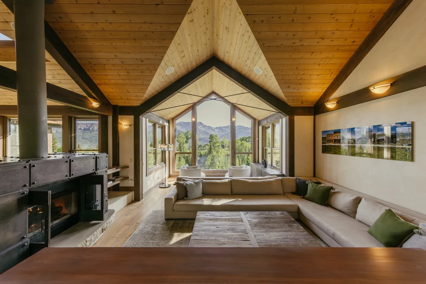 A bright living room has a large sectional seating area beneath a peaked wooden ceiling.