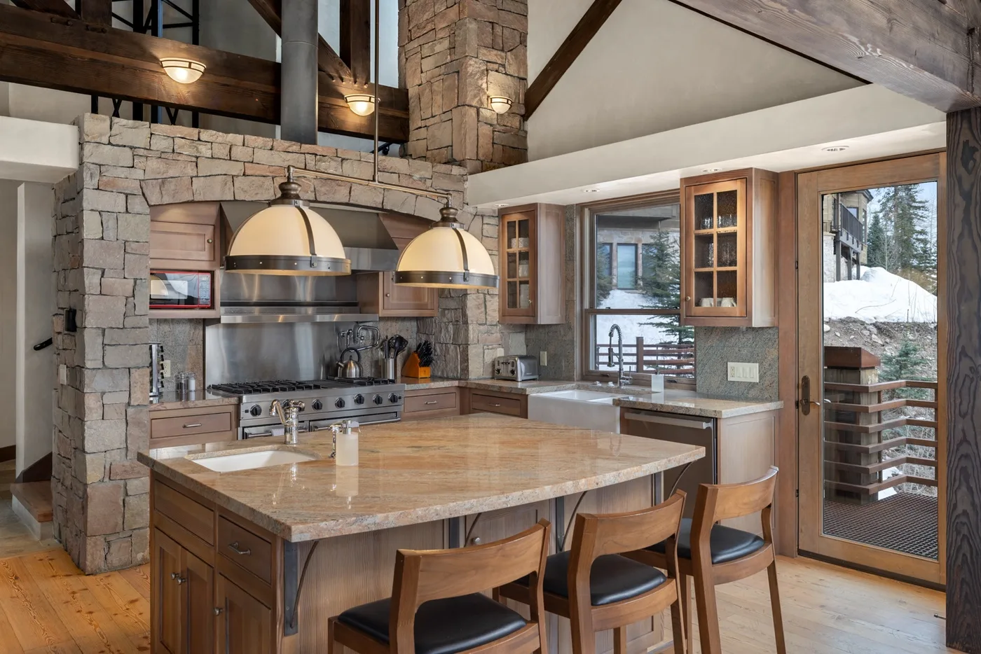A spacious kitchen with a large central island, wood cabinets, and stone walls.