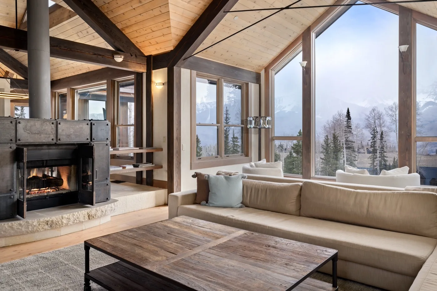 A living room with a fireplace, seating, and large windows overlooking a snowy landscape.