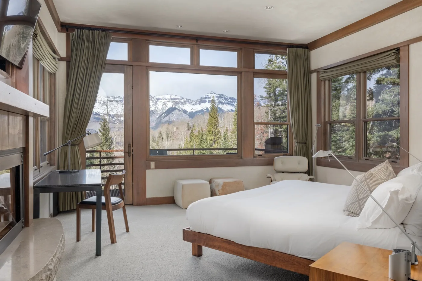 A bedroom with a large bed beside windows overlooking a mountain landscape.