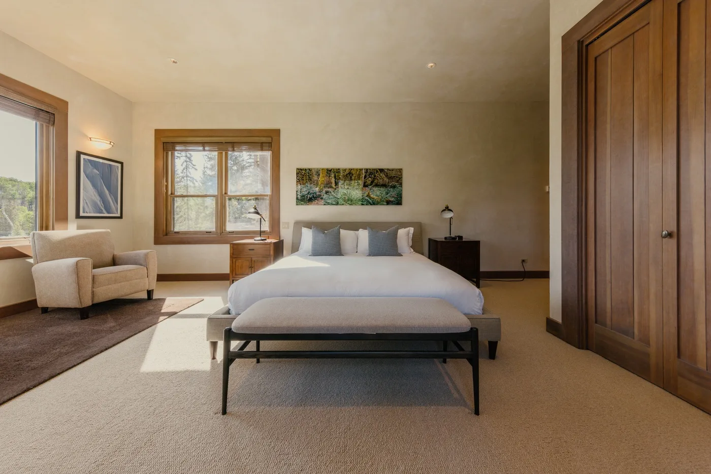 A bedroom with a bed, an armchair, and windows letting in daylight.