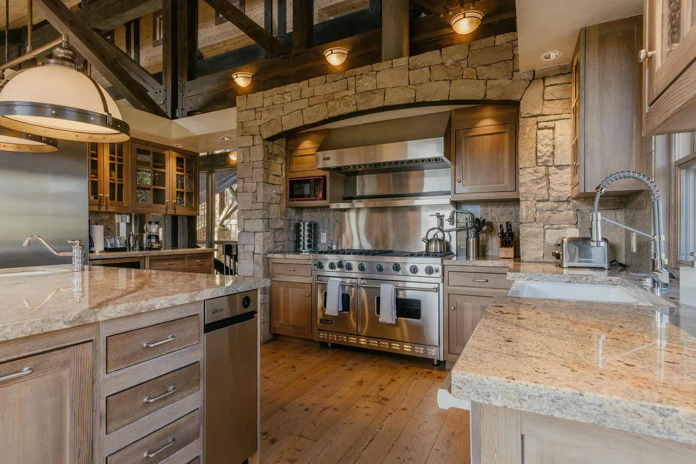 A spacious kitchen with stone walls, wood cabinetry, and a large stainless-steel range.