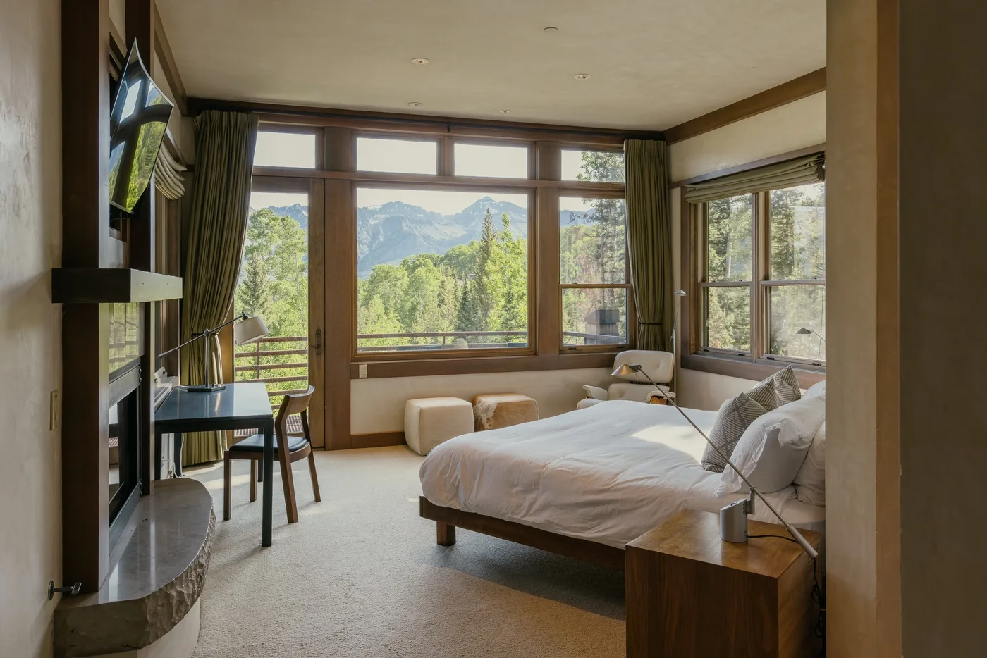A bedroom with a bed, seating, and large windows overlooking a mountain landscape.