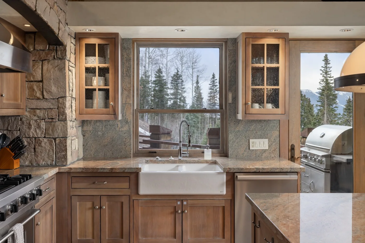 A kitchen with wooden cabinets, a sink, and windows overlooking trees.