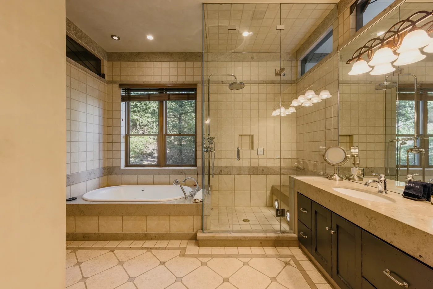 A tiled bathroom with a bathtub, glass shower, and long vanity.