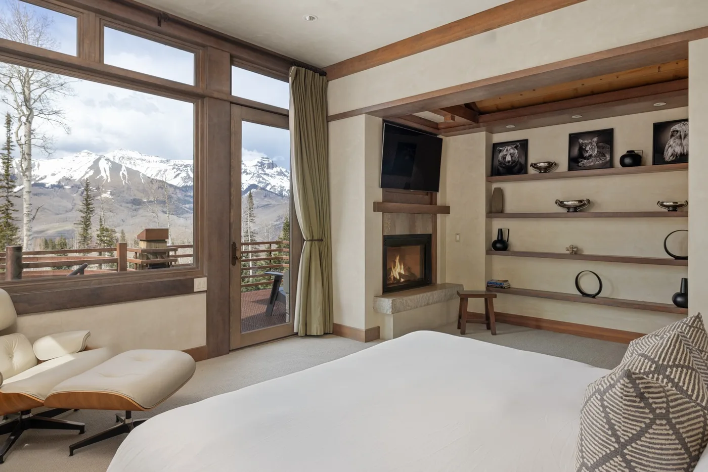 A bedroom with a large bed, lounge seating, and windows overlooking a mountain landscape.