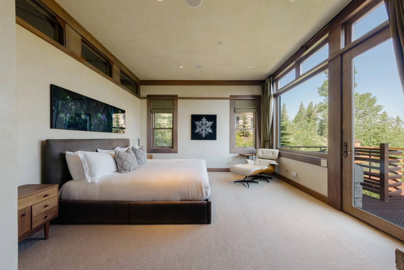 A bright bedroom with a large bed and wide windows overlooking trees.
