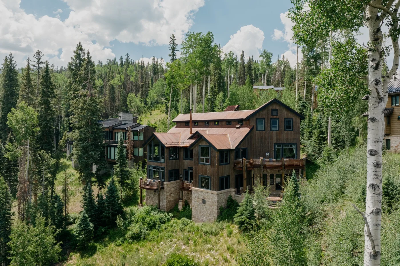 Wooden lodge buildings sit among trees on a forested hillside.
