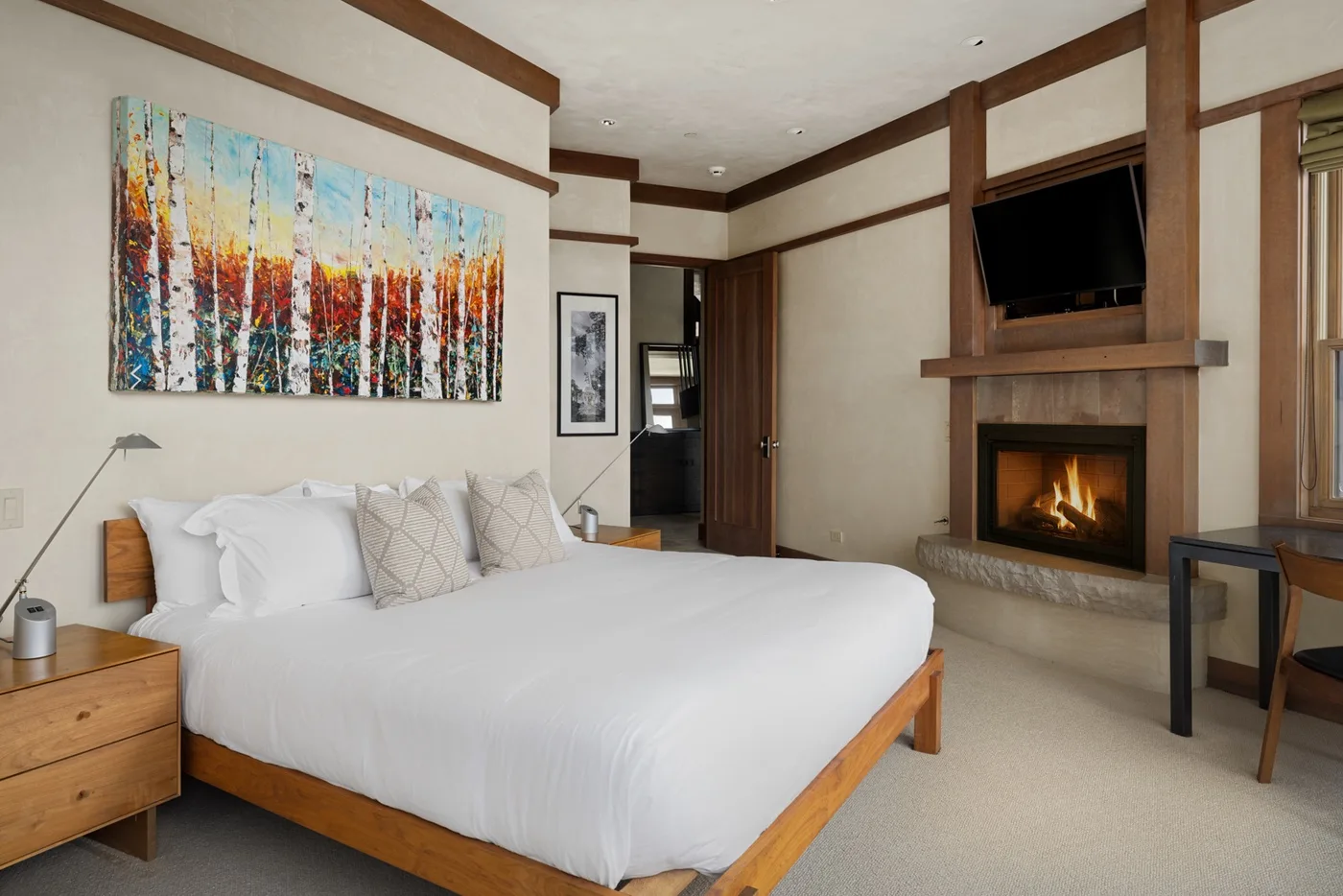 A bedroom with a neatly made bed and a fireplace beneath a wall-mounted television.