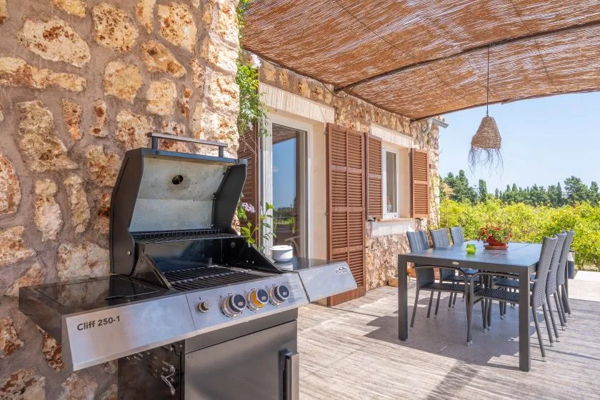A shaded outdoor dining area with a table, seating, and a barbecue grill.