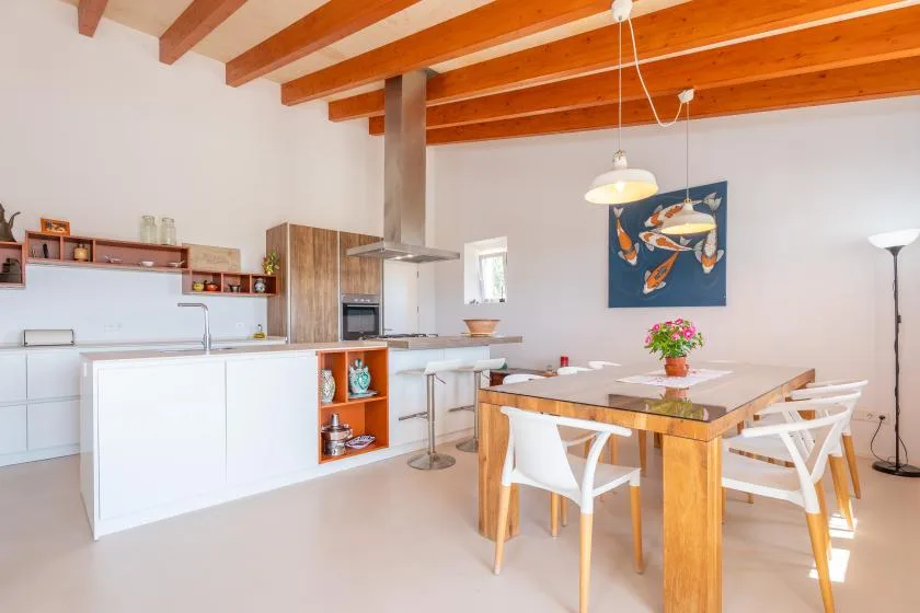 A bright open kitchen and dining area with a wooden table beneath exposed ceiling beams.