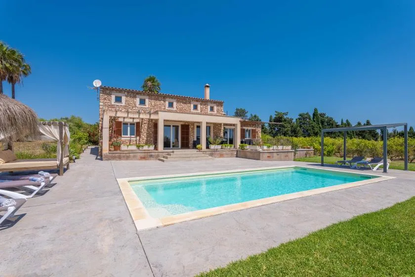 A swimming pool and paved patio sit in front of a stone house.