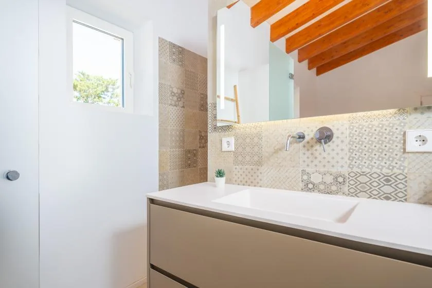 A bright bathroom with a wide sink, patterned tile, and a large mirror.
