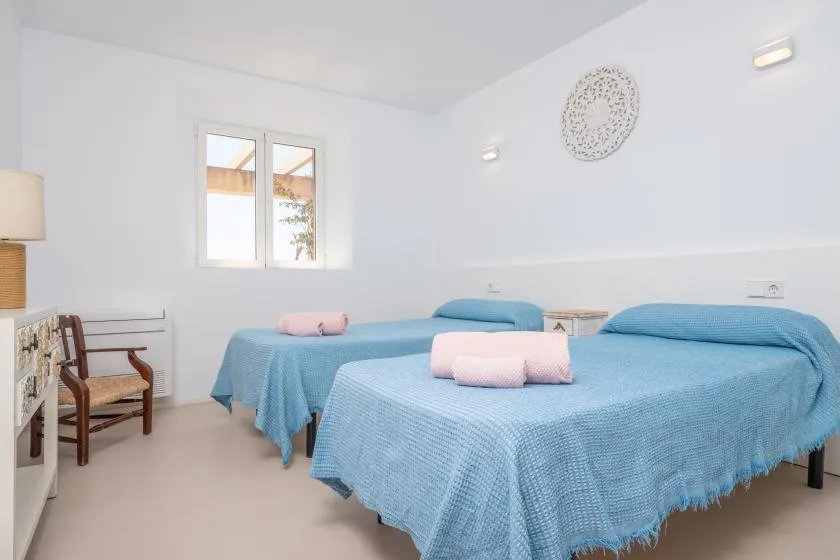 A bright bedroom with two beds covered in blue bedspreads.