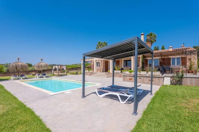 An outdoor swimming pool beside a house, with a shaded seating area.