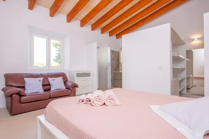A bedroom with a pink bed and a leather sofa beneath exposed wooden beams.