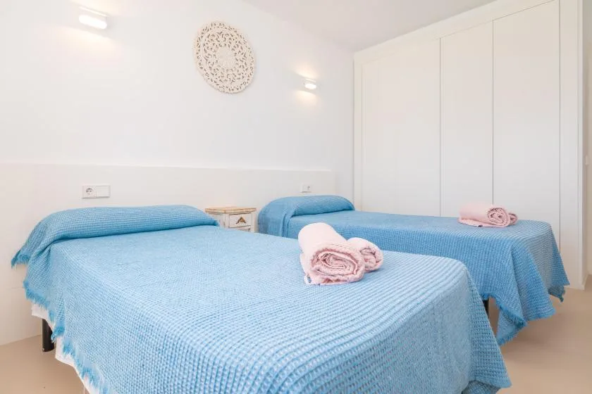 A bright bedroom with two beds covered in blue bedspreads and folded towels.