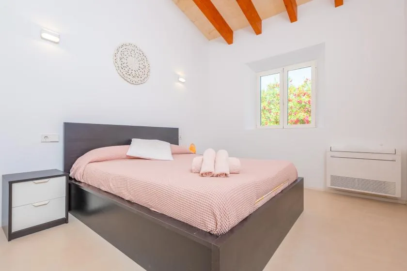 A bright bedroom with a bed dressed in pink bedding beneath exposed ceiling beams.
