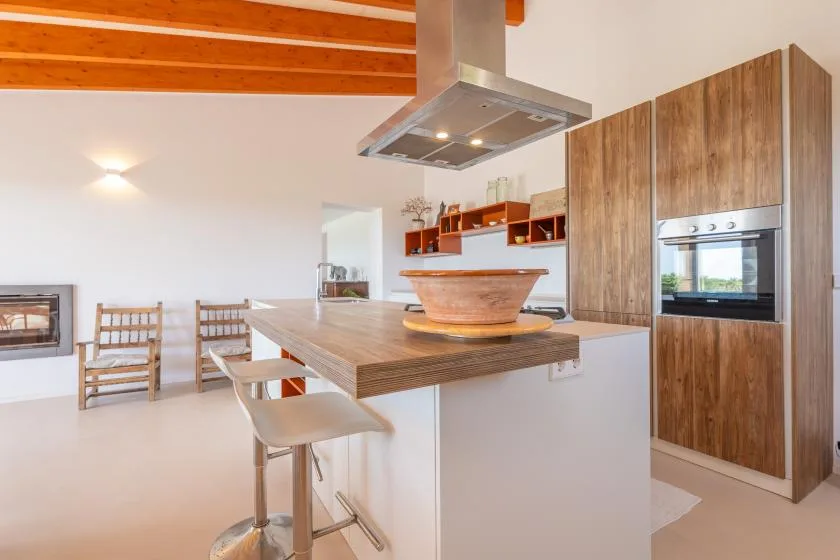 A modern kitchen with a broad island and wooden ceiling beams.