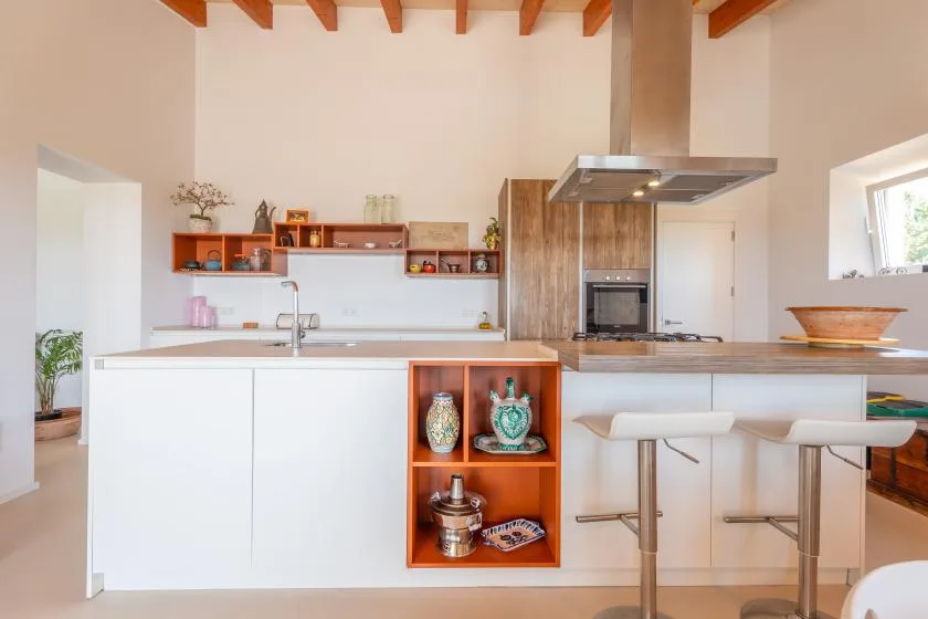 A bright kitchen with a central island, open shelves, and exposed ceiling beams.