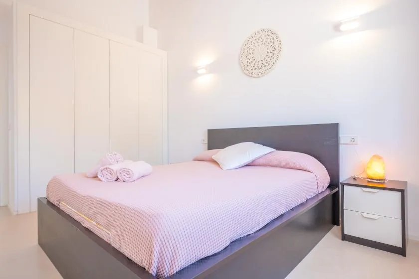 A bedroom with a bed dressed in pale pink bedding and a dark headboard.
