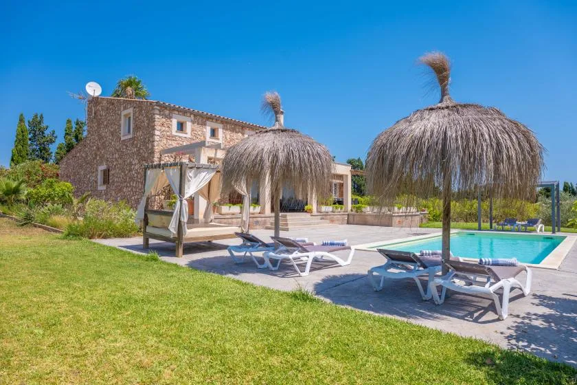 A swimming pool beside a stone building, with sun loungers on the patio.