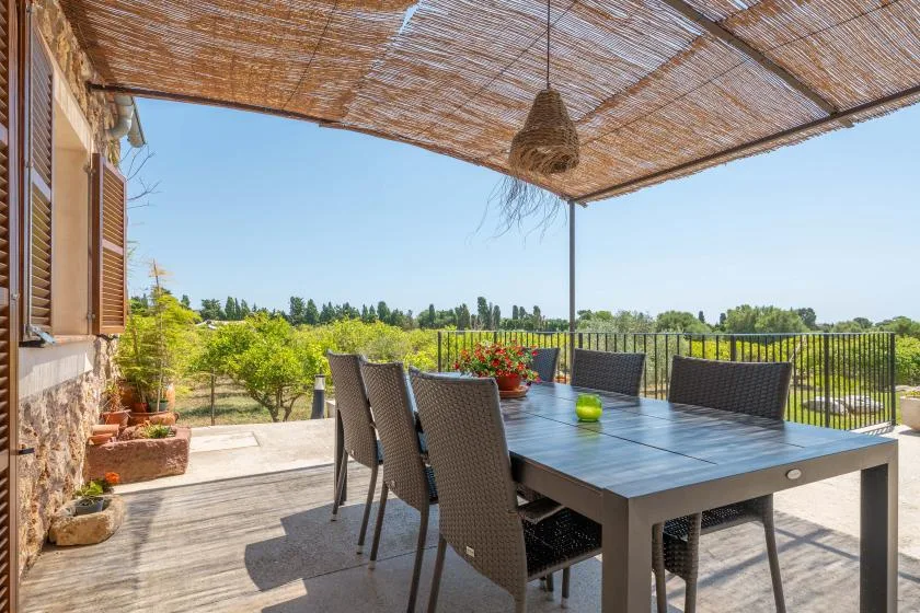 A shaded outdoor dining area with a table and seating overlooks greenery.