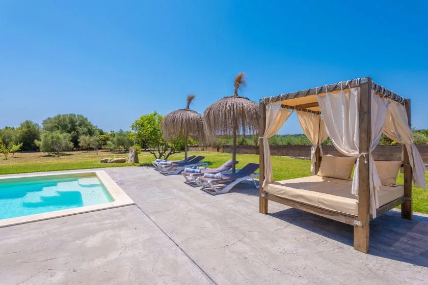 An outdoor pool beside lounge seating and a shaded canopy bed.
