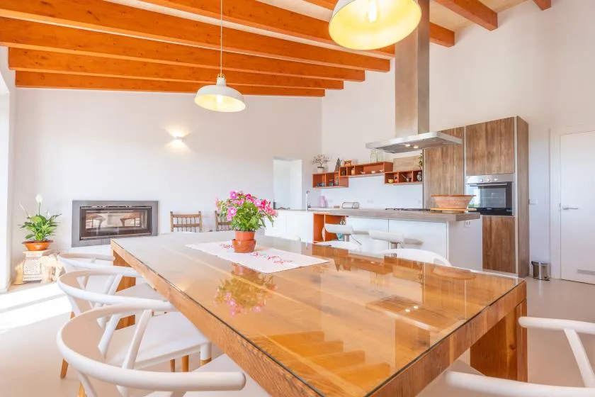 A bright dining area with a long wooden table beside an open kitchen.