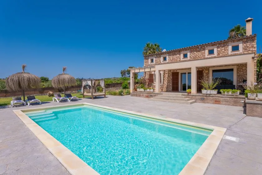 An outdoor swimming pool sits beside a stone-faced house and paved patio.