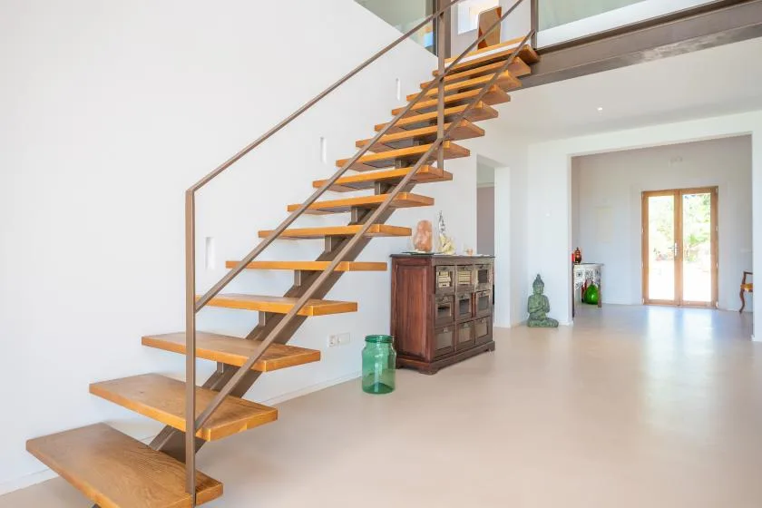 A bright interior with an open staircase and a wooden cabinet.
