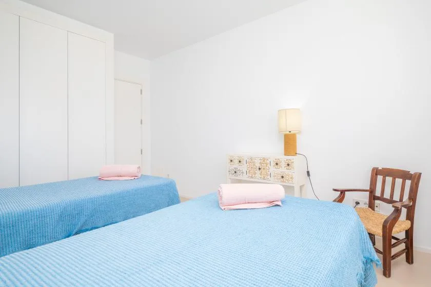 A bedroom with two beds covered in blue bedspreads and a bedside lamp.