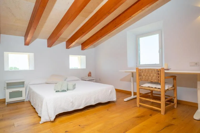 A bright bedroom with a bed, desk, and exposed wooden ceiling beams.
