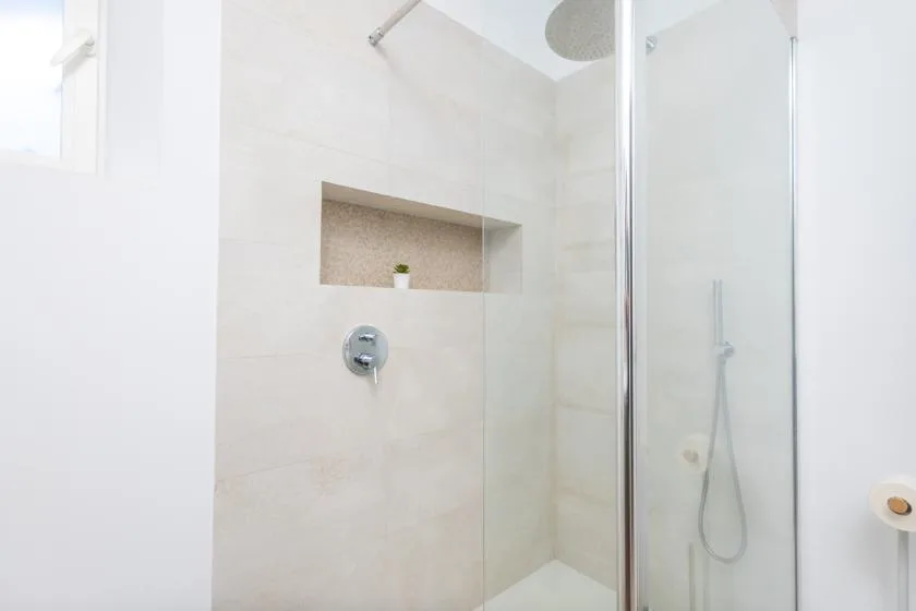 A tiled shower with a recessed shelf and handheld showerhead.