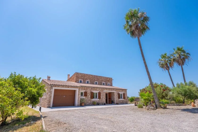 A stone house stands beside a gravel driveway beneath a clear blue sky.