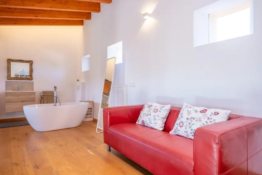 A bright room with a red sofa, freestanding bathtub, and wooden ceiling beams.