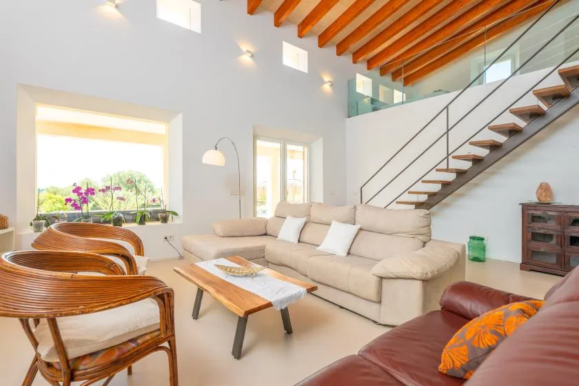 A bright living room with seating, a wooden coffee table, and an open staircase.