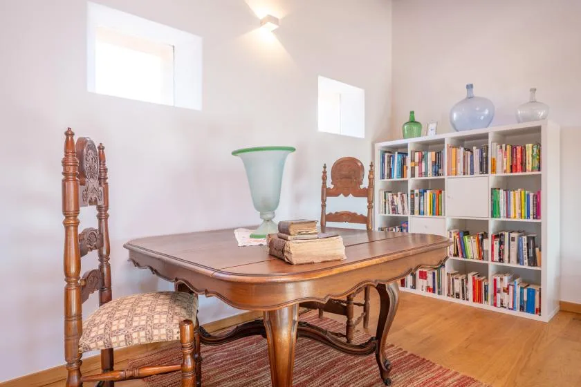 A study with a wooden table, chairs, and a bookcase filled with books.