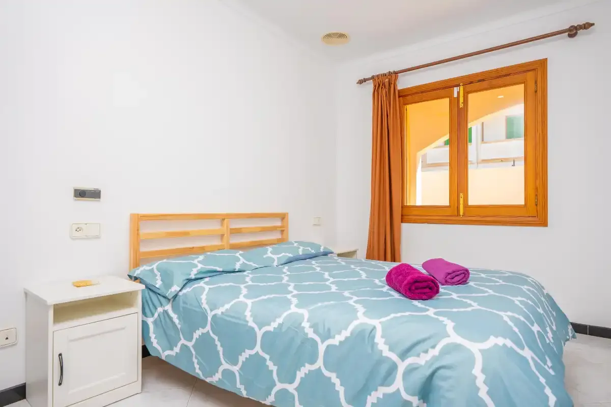 A bedroom with a bed dressed in blue patterned bedding beside a window.
