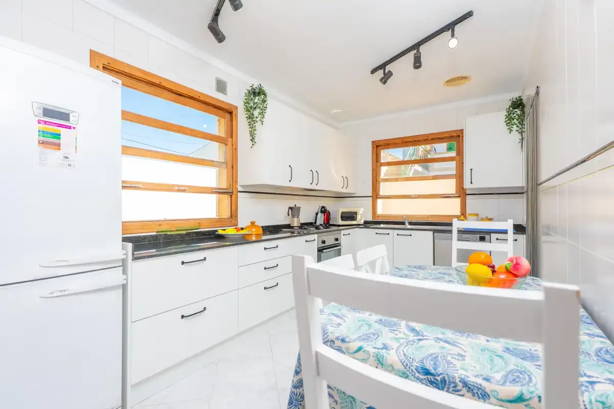 A bright kitchen with white cabinets, wooden-framed windows, and a dining table.