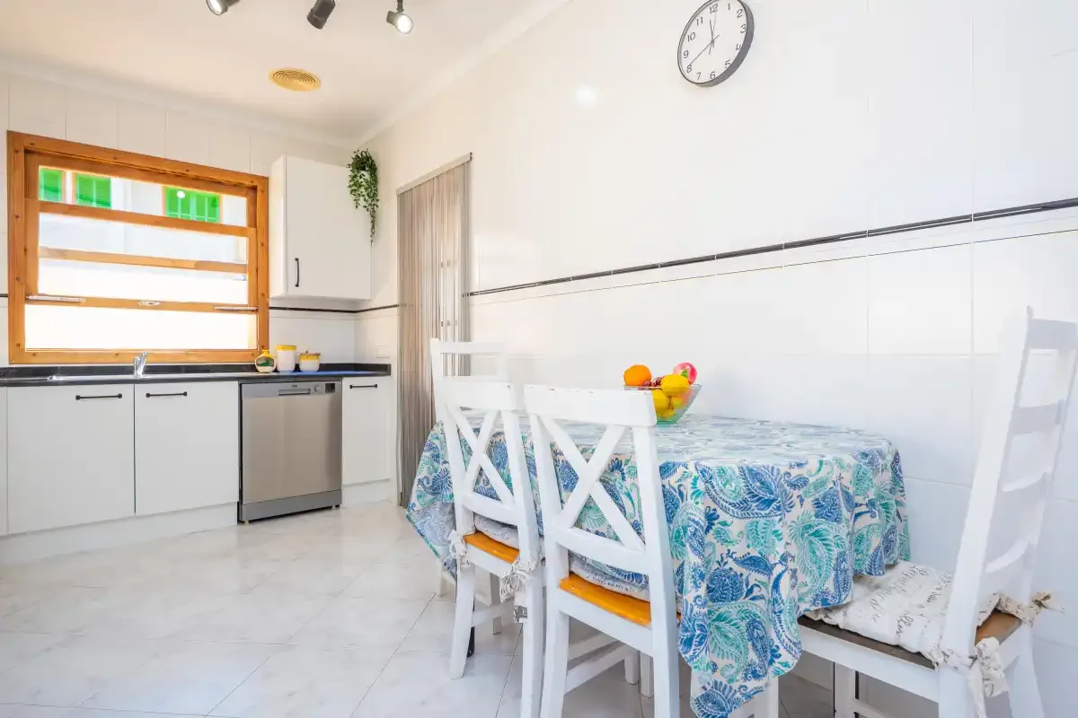 A bright dining area with a patterned tablecloth and white chairs.