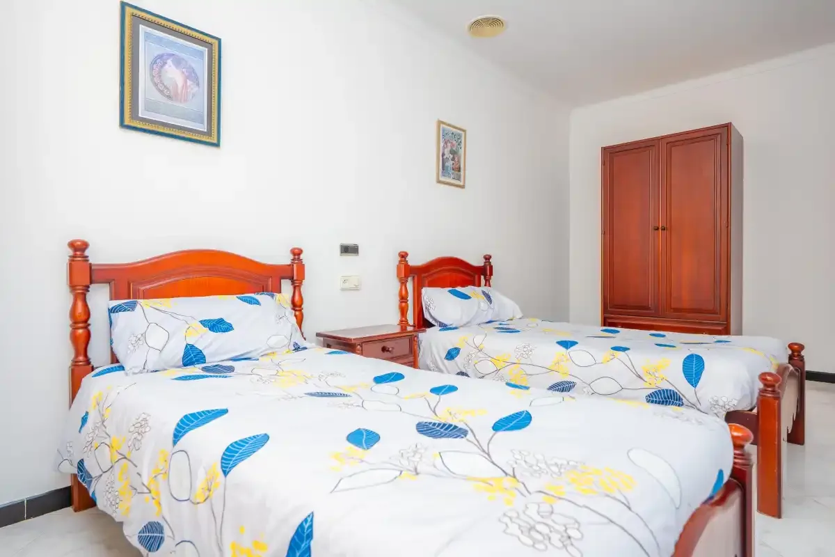 A bedroom with two beds dressed in white bedding with blue and yellow patterns.