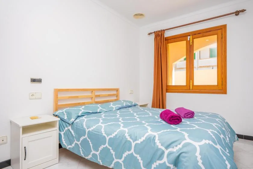 A bedroom with blue patterned bedding and a wooden-framed window.