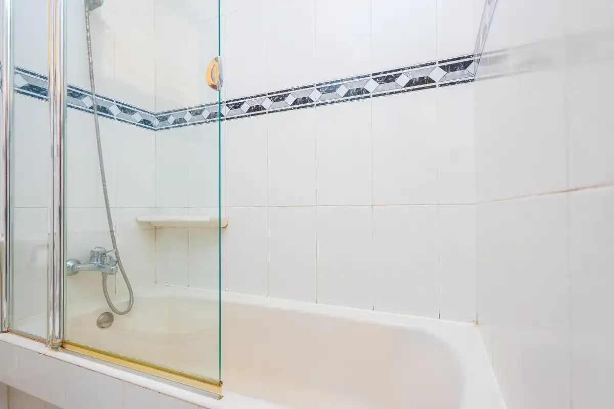 A tiled bathroom shower with a handheld showerhead and glass screen.