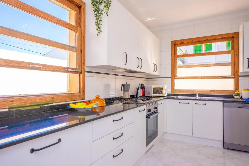 A bright kitchen with white cabinets, dark countertops, and wood-framed windows.